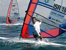 A young man surfing on a windsurf board in the sea, with another surfer in the background