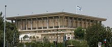 A short box-like building topped with Israeli flags and supported by modern concrete columns